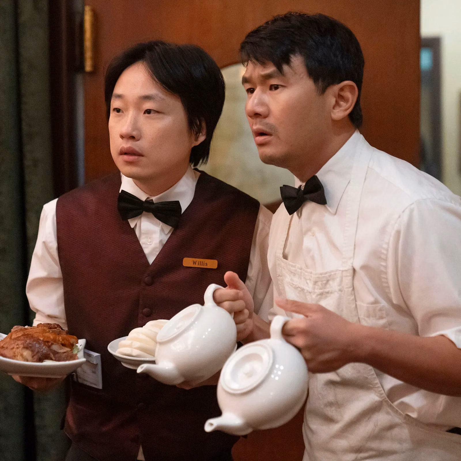 Still from Interior Chinatown: two restaurant workers in bow ties carrying teapots and dishes