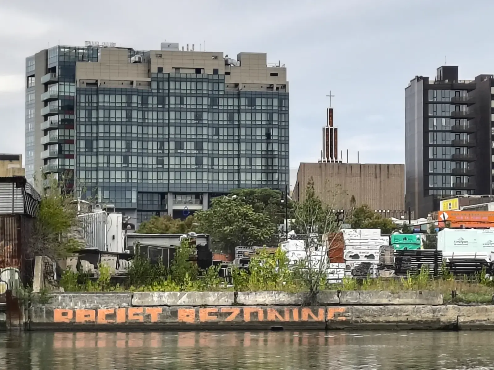 Scripting Flushing Bay — graffiti reading &ldquo;Racist Rezoning&rdquo; across Flushing Creek