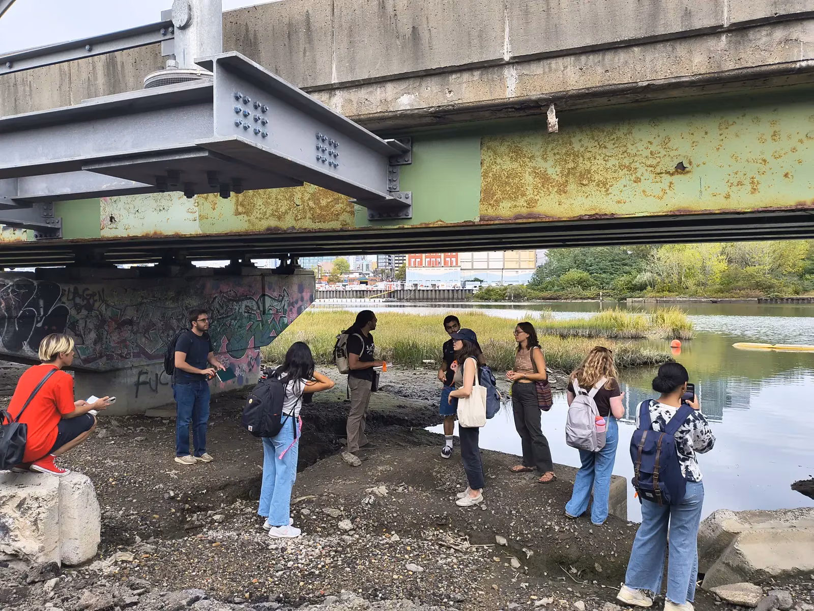 Students listening to Cody Herrmann at the water's edge under the highway