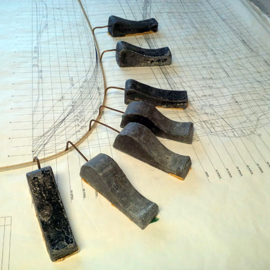 A row of ducks fairing a wooden spline batten across hull lines